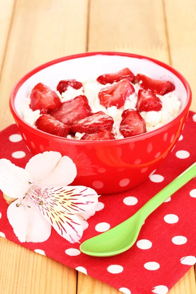 Hüttenkäse in roter Schüssel mit Erdbeeren in Scheiben auf Holztisch — Stockfoto