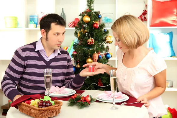 Young happy couple with presents sitting at table near Christmas tree — Stock Photo, Image