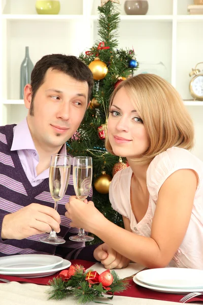 Jonge gelukkige paar bril met champagne bedrijf aan tafel in de buurt van de kerstboom — Stockfoto