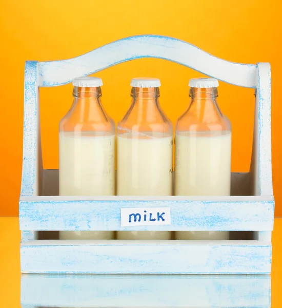 Milch in Flaschen in Holzkiste auf orangefarbenem Hintergrund — Stockfoto