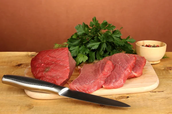 Сырое мясо говядины со специями на деревянном столе на коричневом фоне — стоковое фото