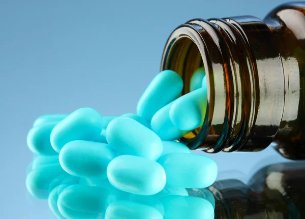 Pílulas em garrafa, no fundo azul — Fotografia de Stock