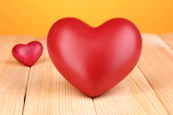 Decorative red hearts on wooden table on orange background — Stock Photo, Image