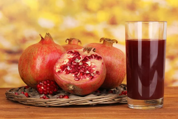 Ripe pomegranates on wicker cradle with glass of pomegranate juice on wooden table on autum background — Stock Photo, Image