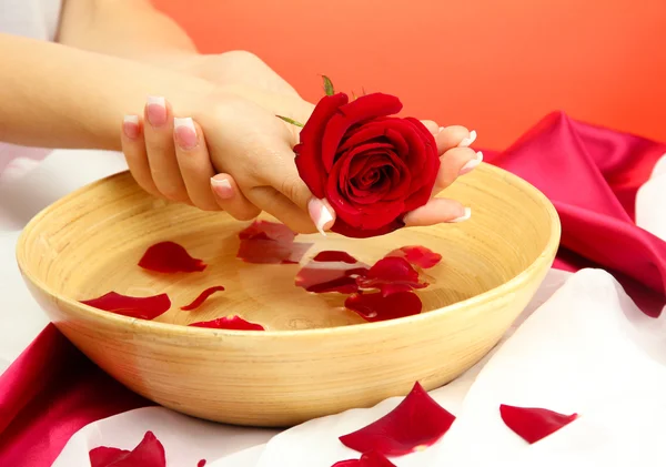 Woman hands with wooden bowl of water with petals, on red background — Stock Photo, Image