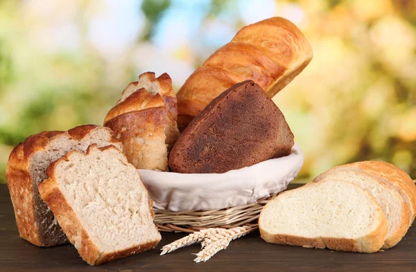 Pane fresco in cesto su tavolo in legno su sfondo naturale — Foto Stock