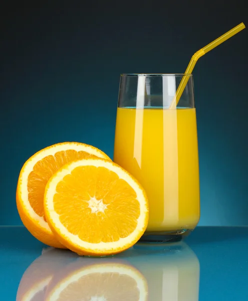 Heerlijke sinaasappelsap in glas en sinaasappelen ernaast op donker blauwe achtergrond — Stockfoto