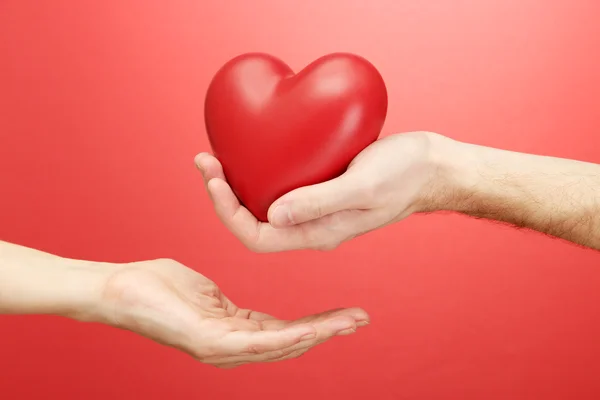 Red heart in woman and man hands, on red background — Stock Photo, Image