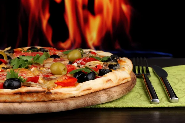火の背景に木製のテーブルにクローズ アップするおいしいピザ — ストック写真