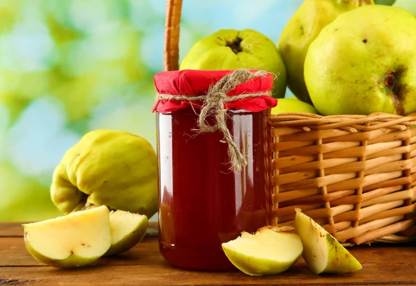 Tarro de mermelada y membrillos con hojas en cesta, sobre fondo verde — Foto de Stock