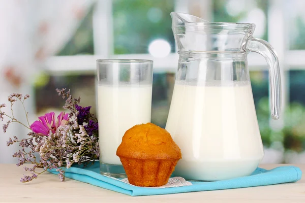 Jarra y vaso de leche con magdalenas sobre mesa de madera sobre fondo de ventana — Foto de Stock