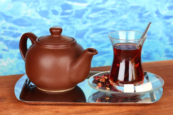 glass of Turkish tea and kettle on color background