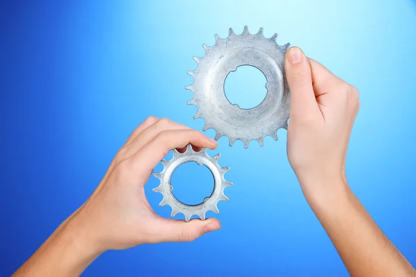 Uomo che tiene ruote dentate metalliche tra le mani su sfondo blu — Foto Stock