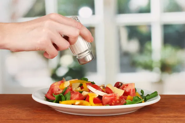 Hand adding salt using salt shaker on bright background — Stock Photo, Image