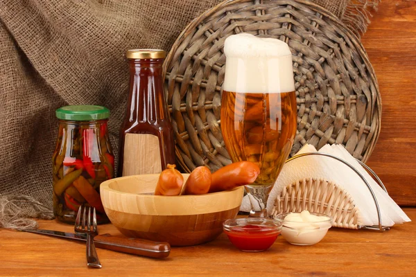 Bière et saucisses grillées sur table en bois sur fond de sac — Photo