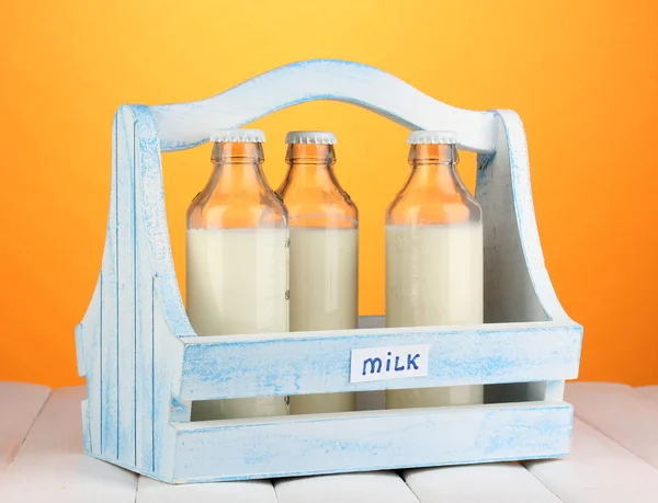 Milch in Flaschen in Holzkiste auf Holztisch auf orangefarbenem Hintergrund — Stockfoto