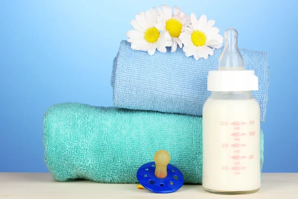 Baby bottle of milk with pacifier and towels on blue background — Stock Photo, Image