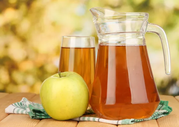 Fullt glas och kanna av äppeljuice och äpple på träbord utomhus — Stockfoto