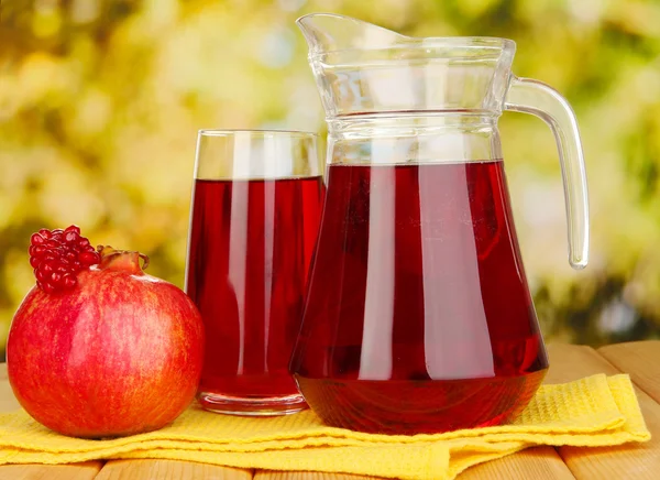 Full glass and jug of pomegranate juice and pomegranate on wooden table outdoor — Stock Photo, Image