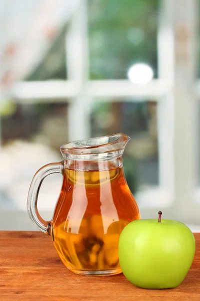 Full jug of apple juice and apple on wooden table on bright background — Stock Photo, Image