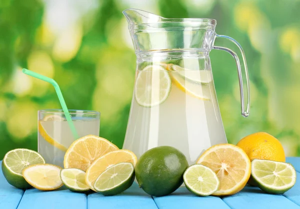 Narenciye limonata sürahi ve bardak narenciye çevresinde doğal ahşap masa mavi zemin üzerinde — Stok fotoğraf