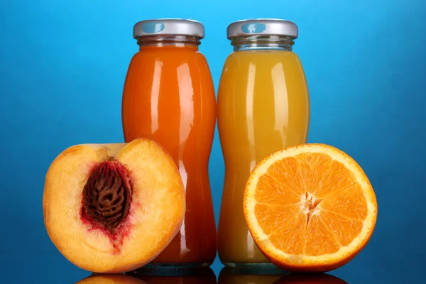 Délicieux jus d'orange et de pêche en bouteille et orange et pêche à côté sur fond coloré — Photo