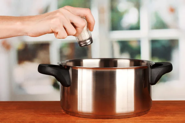 Hand adding salt using salt shaker on bright background — Stock Photo, Image