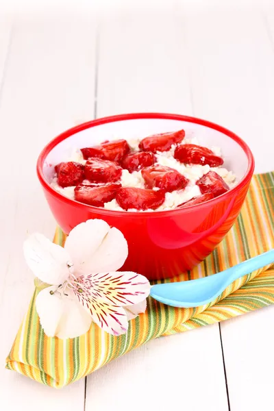 Τυρί cottage σε κόκκινο μπολ με φέτες τις φράουλες στο λευκό ξύλινο τραπέζι — Φωτογραφία Αρχείου