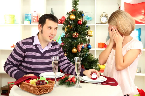 Νεαρός άνδρας κάνει πρόταση να παντρευτεί το κορίτσι στο τραπέζι κοντά χριστουγεννιάτικο δέντρο — Φωτογραφία Αρχείου