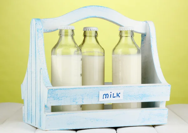 Milk in bottles in wooden box on wooden table on green background — Stock Photo, Image