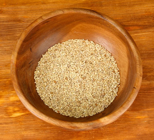 Raw buckwheat in wooden bowl on table on brown background — Stock Photo, Image