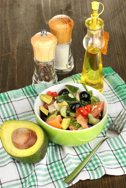 Leckerer Avocadosalat in Schüssel umgeben von Gewürzen auf Holztisch in Großaufnahme — Stockfoto