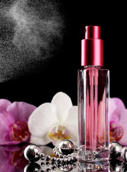 Perfume feminino em bela garrafa e flores de orquídea, no fundo preto — Fotografia de Stock