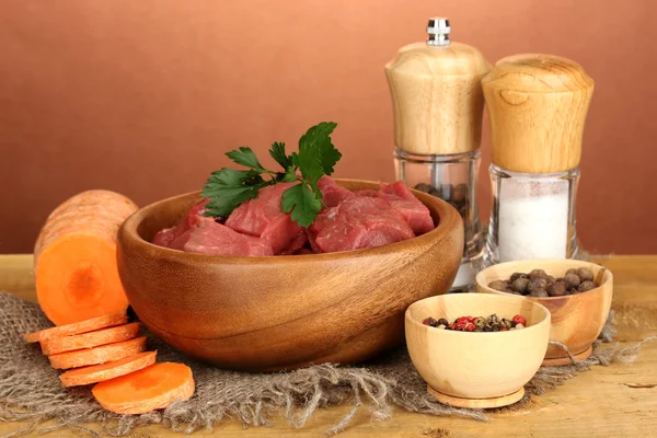 Raw beef meat marinated with herbs and spices on wooden table on brown background — Stock Photo, Image