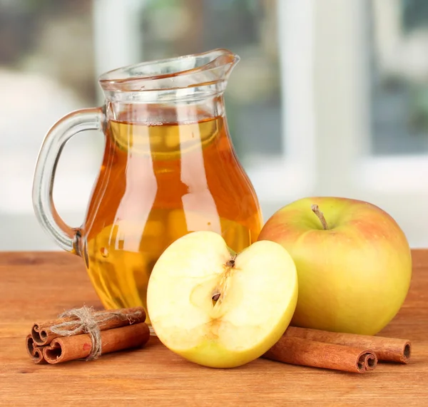 Jarro cheio de suco de maçã e maçã na mesa de madeira no fundo brilhante — Fotografia de Stock