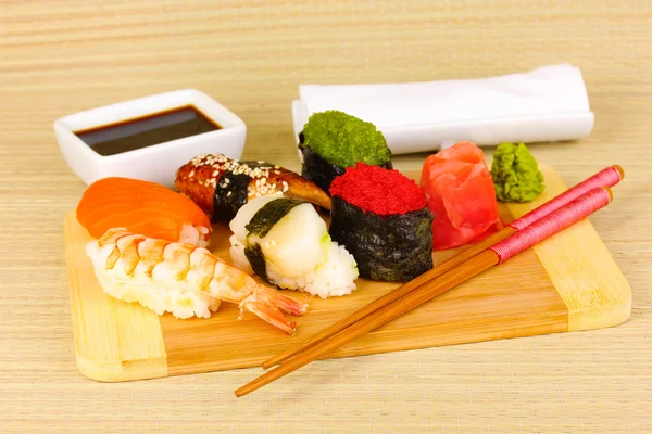 Delicious sushi served on wooden board on bamboo mat — Stock Photo, Image