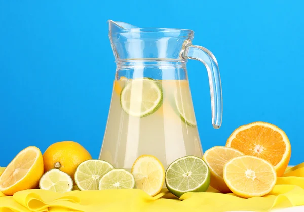 Zitruslimonade im Glaskrug aus Zitrusfrüchten auf gelbem Stoff auf blauem Hintergrund — Stockfoto