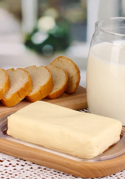 Butter on wooden holder surrounded by bread and milk on window background close-up — Stock Photo, Image