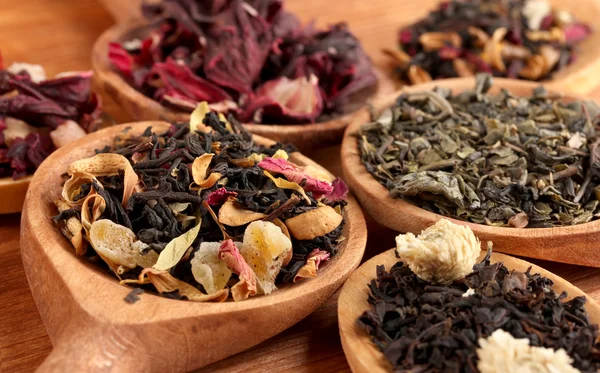 Assortment of dry tea in spoons, on wooden background — Stock Photo, Image