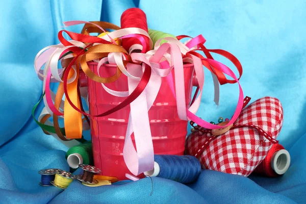 Color bucket with multicolor ribbons and thread on blue fabric background — Stock Photo, Image