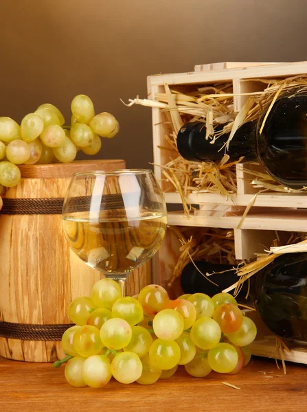 Boîtier en bois avec bouteille de vin, tonneau, verre à vin et raisin sur table en bois sur fond marron — Photo