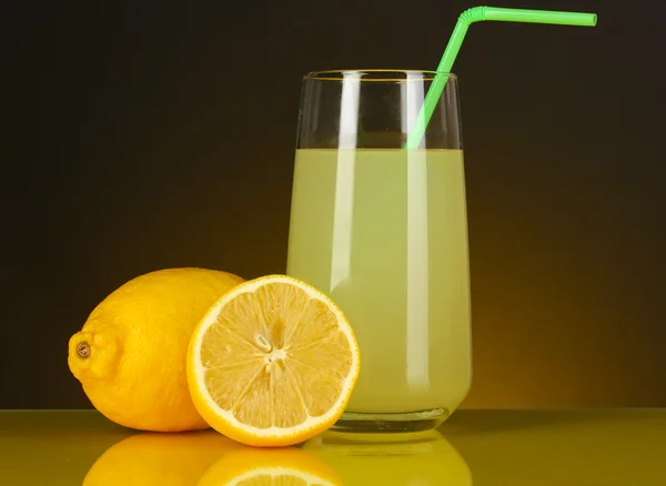 Sumo de limão delicioso em vidro e limões ao lado dele no fundo laranja escuro — Fotografia de Stock