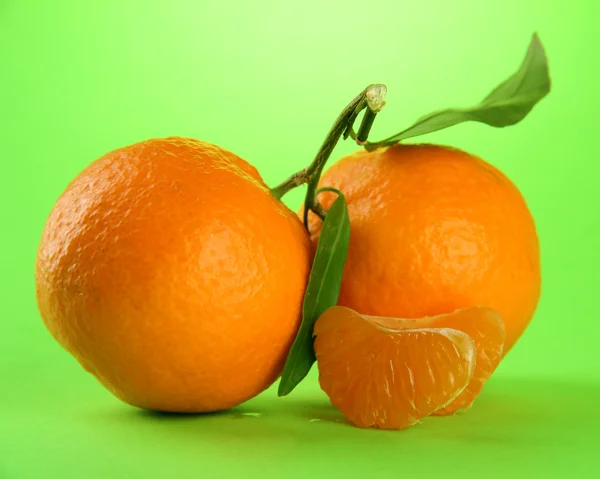 Reife süße Mandarinen mit Blättern, auf grünem Hintergrund — Stockfoto