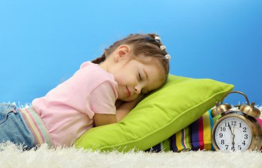 mavi arka plan üzerinde renkli yastıklar üzerinde uyuyan sevimli küçük kız