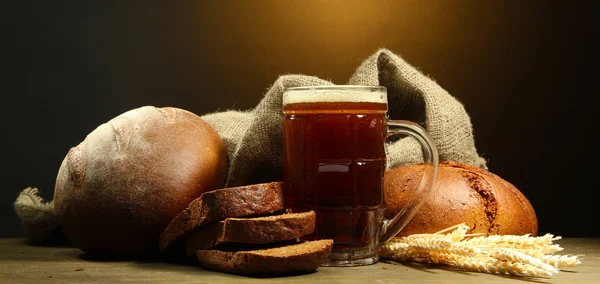 Tankard svagdricka och råg bröd med öron, på träbord på brun bakgrund — Stockfoto
