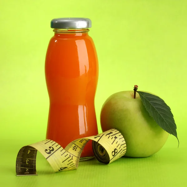 Bottle of juice, apple and measuring tape, on green background — Stock Photo, Image