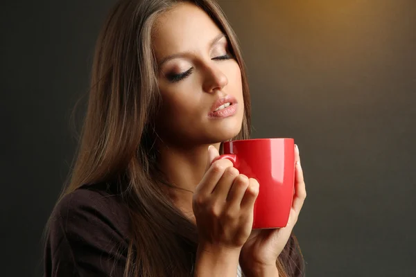 Mooie jonge vrouw met een kopje koffie, op bruine achtergrond — Stockfoto