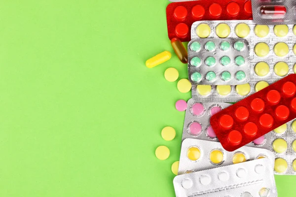 Cápsulas y pastillas empaquetadas en ampollas sobre fondo verde — Foto de Stock