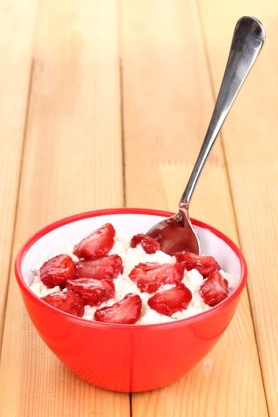 Hüttenkäse in roter Schüssel mit Erdbeeren in Scheiben auf Holztisch — Stockfoto