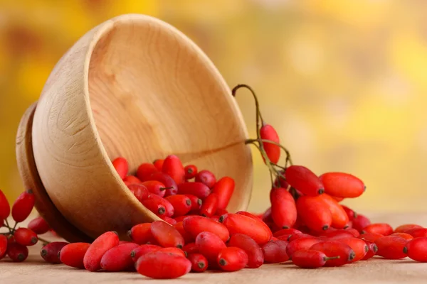 Ripe barberries in wooden bowl, on table, on yellow background — Stock Photo, Image